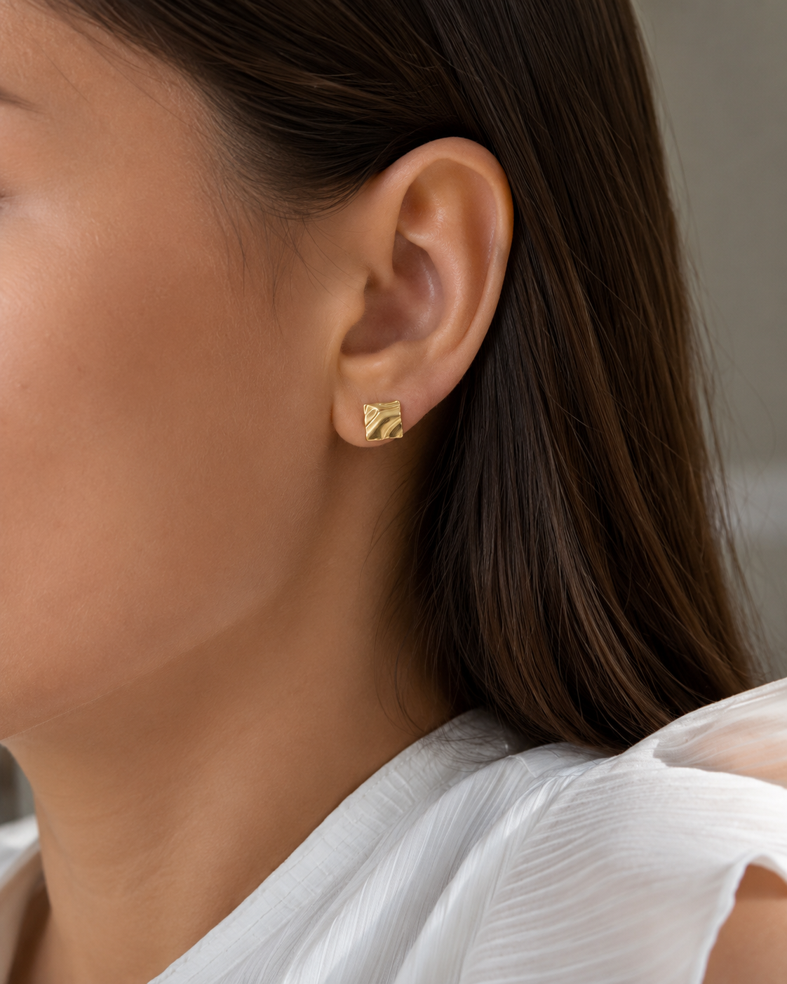 Model wearing the Carré Studs — textured square gold studs with a molten finish — Zoé Jewelry.