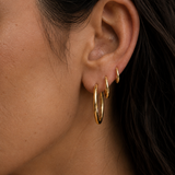 Model wearing Classic Hoops in small, medium, and large stacked up the ear — slim 18K gold hoops that step up in size — Zoé Jewelry