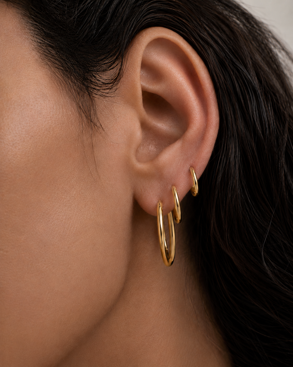 Model wearing Classic Hoops in small, medium, and large stacked up the ear — slim 18K gold hoops that step up in size — Zoé Jewelry
