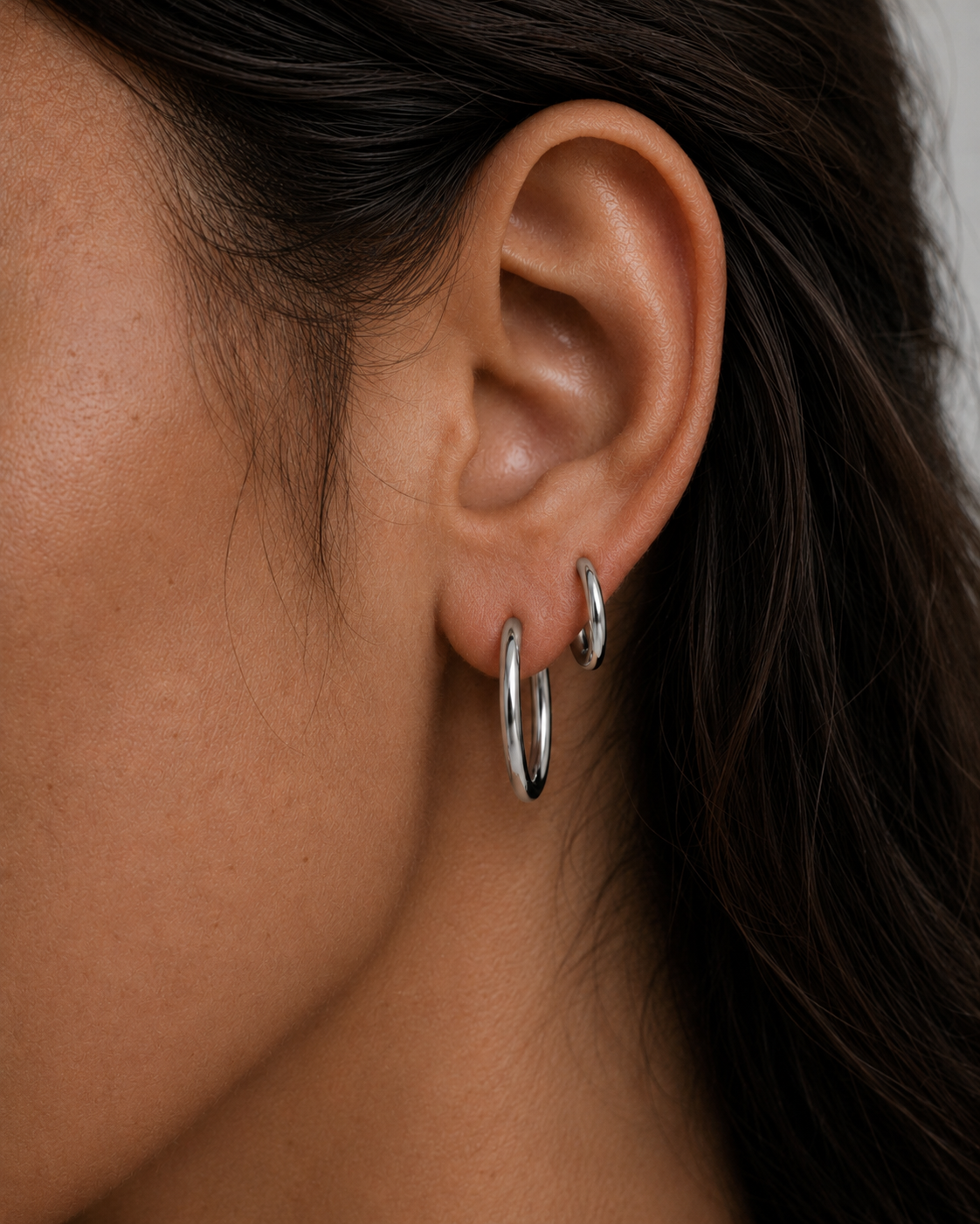 Model wearing Classic Silver Hoops in small and medium stacked on the ear — slim rhodium-plated silver hoops from Zoé Jewelry.