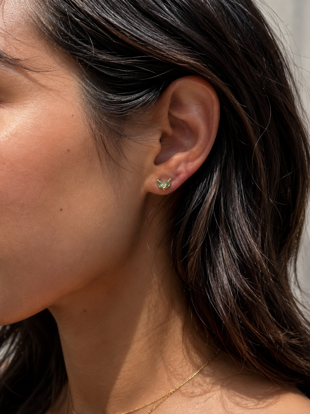 Model wearing the Ember Studs — dainty petal-shaped gold studs with a green stone — Zoé Jewelry.