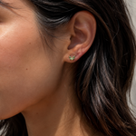 Model wearing the Ember Studs — dainty petal-shaped gold studs with a green stone — Zoé Jewelry.