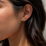 Model wearing the Ember Studs — dainty petal-shaped gold studs with a green stone — Zoé Jewelry.