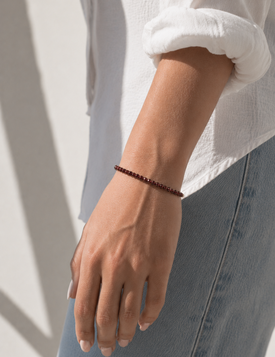Model wearing the Garnet Bracelet, faceted deep-red garnet gemstone beads on an 18K gold-plated chain, Zoé Jewelry.