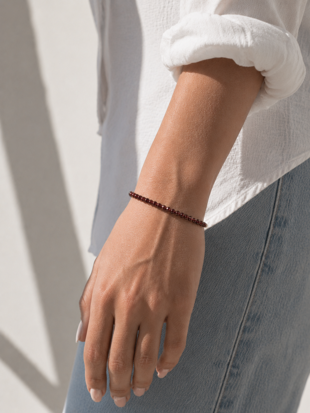 Model wearing the Garnet Bracelet, faceted deep-red garnet gemstone beads on an 18K gold-plated chain, Zoé Jewelry.