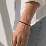 Model wearing the Garnet Bracelet, faceted deep-red garnet gemstone beads on an 18K gold-plated chain, Zoé Jewelry.