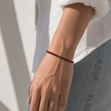 Model wearing the Garnet Bracelet, faceted deep-red garnet gemstone beads on an 18K gold-plated chain, Zoé Jewelry.