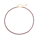 Dainty necklace of small deep red faceted gemstone beads on a fine strand with clasp and Zoé tag, on white background.
