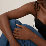 Model wearing a dainty gold chain bracelet with flower stations and pearl accents on the wrist, in 18k gold plating, soft natural light.