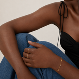 Model wearing a dainty gold chain bracelet with flower stations and pearl accents on the wrist, in 18k gold plating, soft natural light.
