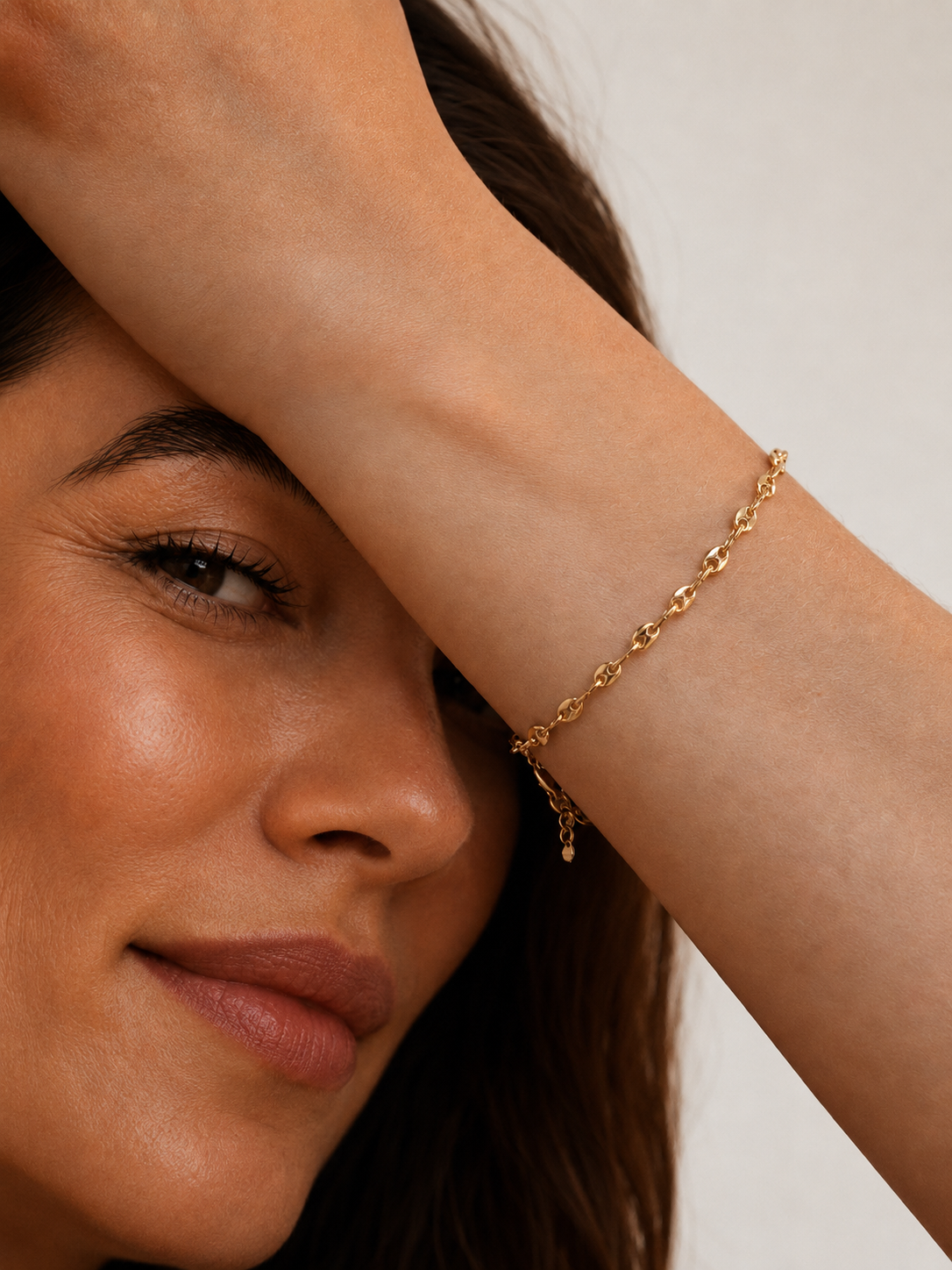 Model wearing a gold mariner-link chain bracelet with puffed coffee-bean links on the wrist, in 18k gold plating, soft warm natural light.