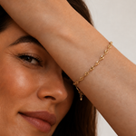 Model wearing a gold mariner-link chain bracelet with puffed coffee-bean links on the wrist, in 18k gold plating, soft warm natural light.