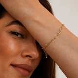 Model wearing a gold mariner-link chain bracelet with puffed coffee-bean links on the wrist, in 18k gold plating, soft warm natural light.