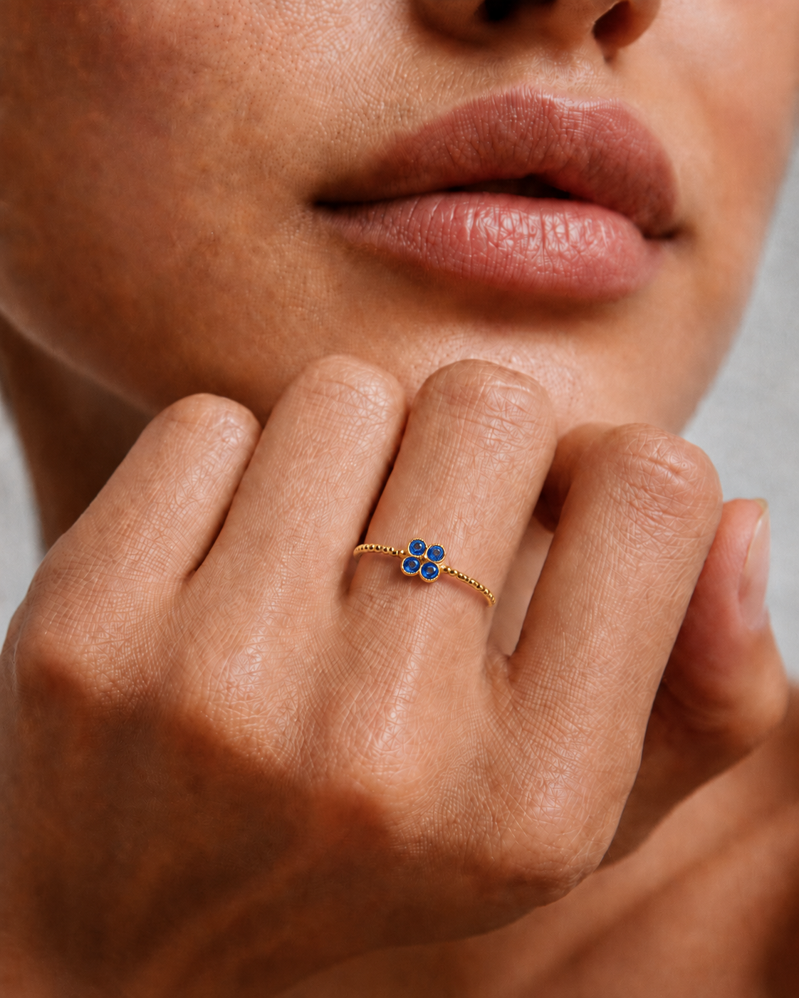 Model wearing a dainty gold beaded ring with a blue cubic zirconia flower on the finger, 18k gold plating.