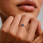 Model wearing a dainty gold beaded ring with a blue cubic zirconia flower on the finger, 18k gold plating.