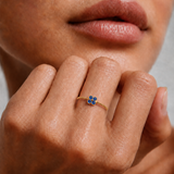 Model wearing a dainty gold beaded ring with a blue cubic zirconia flower on the finger, 18k gold plating.