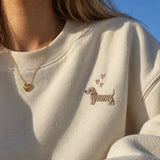 Model wearing a gold heart pendant necklace and classic gold hoop earrings with a cream embroidered sweatshirt.