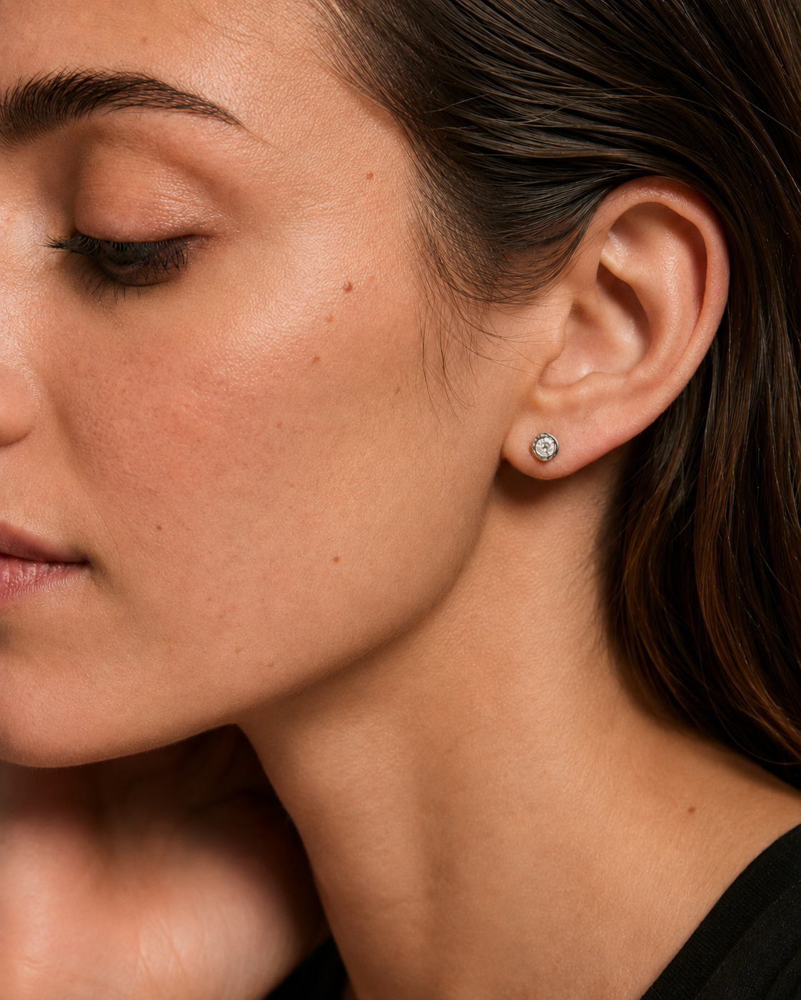 Model wearing silver cubic zirconia molten-bezel stud earrings on the ear, stainless steel.