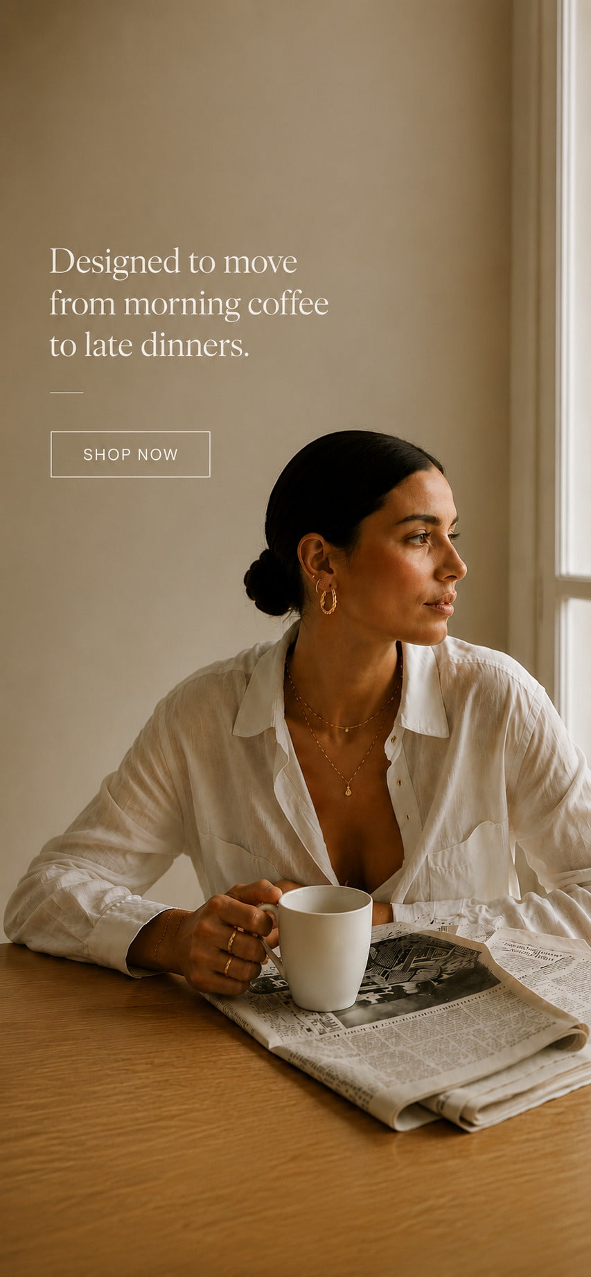  Woman in a white linen shirt wearing Zoé gold hoops and layered necklaces over morning coffee — everyday luxury jewelry.