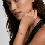 Model wearing a dainty double gold chain bracelet with a pink cubic zirconia heart on the wrist, 18k gold plating.