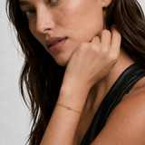 Model wearing a dainty double gold chain bracelet with a pink cubic zirconia heart on the wrist, 18k gold plating.