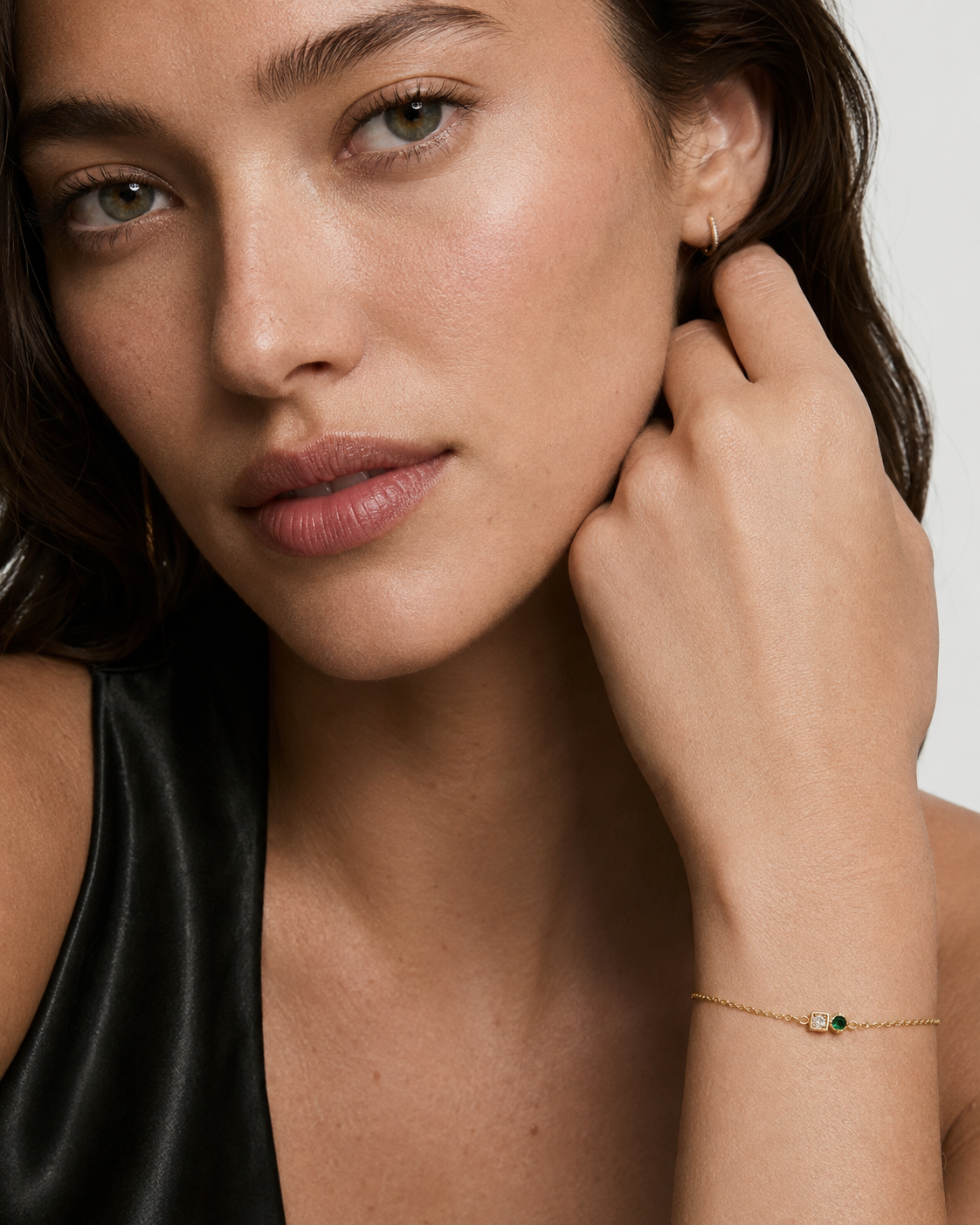 Model wearing a dainty gold chain bracelet with a clear and green cubic zirconia two-stone detail on the wrist, 18k gold plating.