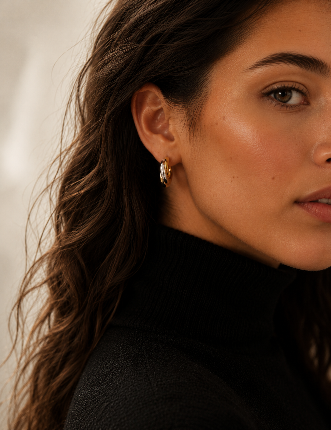Model wearing chunky gold twisted double-strand hoop earrings on the ear, 18k gold plating.