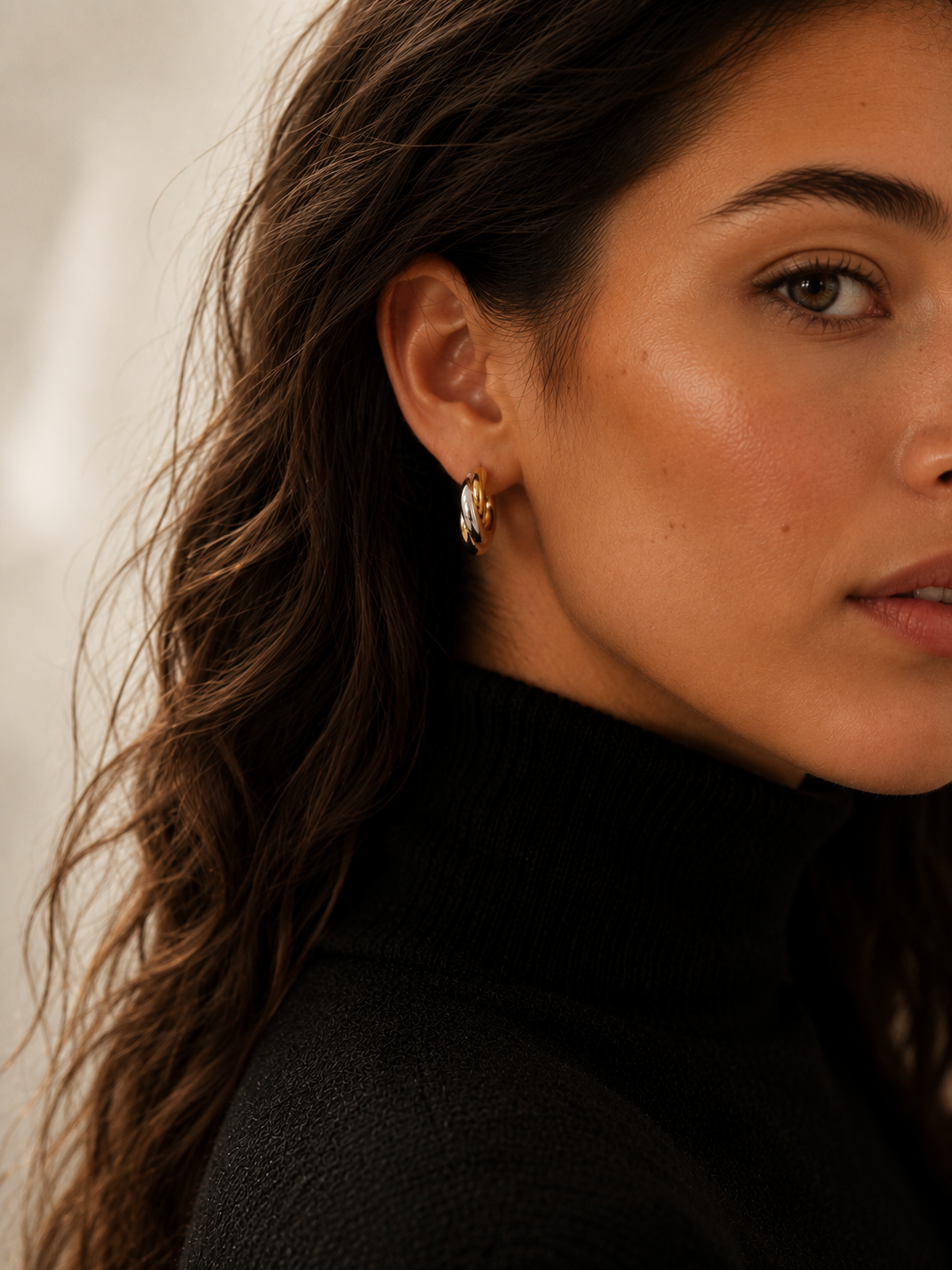 Model wearing chunky gold twisted double-strand hoop earrings on the ear, 18k gold plating.