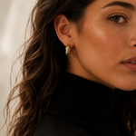 Model wearing chunky gold twisted double-strand hoop earrings on the ear, 18k gold plating.