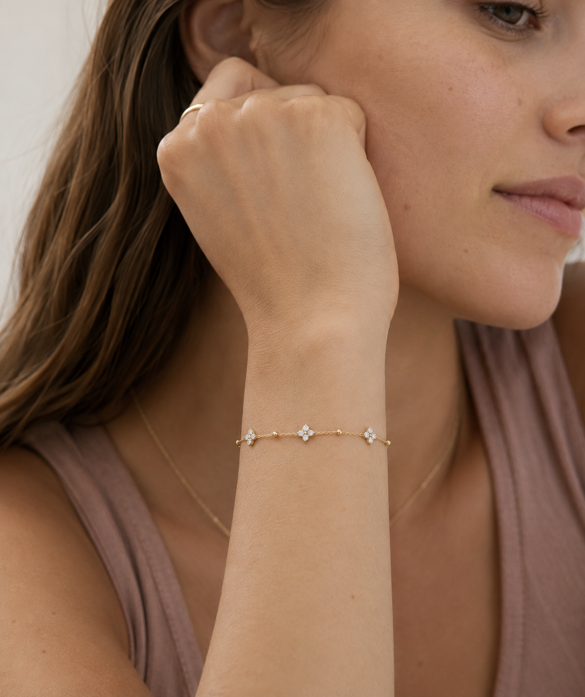 Model wearing a dainty gold beaded chain bracelet with cubic zirconia four-petal flower stations on the wrist, in 18k gold plating, soft natural light.