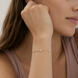 Model wearing a dainty gold beaded chain bracelet with cubic zirconia four-petal flower stations on the wrist, in 18k gold plating, soft natural light.