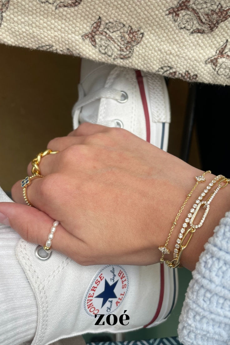Customer wearing a layered Zoé bracelet and ring stack, resting on white sneakers — Zoé On You.